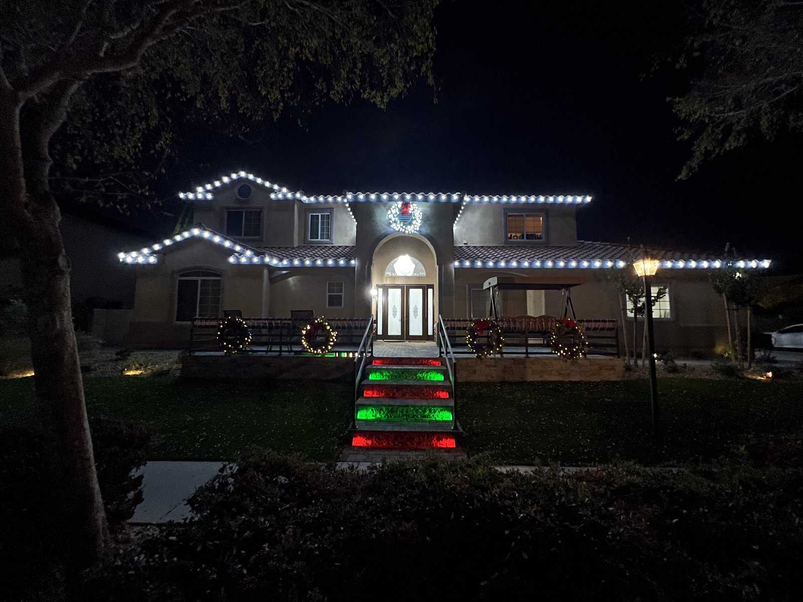 Pure white Christmas lights installed on roofline with pure white lit christmas wreaths and red and green lit steps